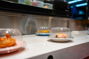 various types of sushi on conveyor belt in a Japanese restaurant. Shushi Go Round is a famous form of fast food in Asia, also known as sushi train.