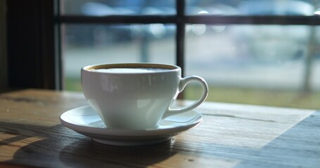 Coffee drink in small white cup on wooden table at morning sunlight closeup. Gourmet energetic beverage of organic ingredients near cafe window