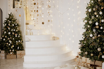 A large Christmas tree in the living room, decorated with garlands and light balloons. Bright Christmas interior with a white staircase