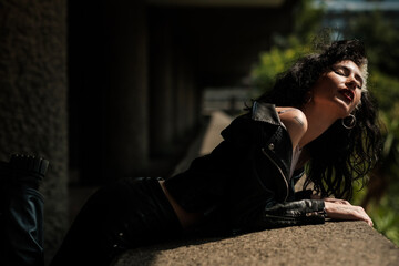 Female rock star leaning on concrete banister and enjoying sunlight.