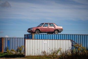 old classic rusty car standing on containers in front of a car scrap yard. scrapyard decoration. © Adam
