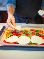 young man putting white cheese on a pizza with fresh tomatoes and basil leaves