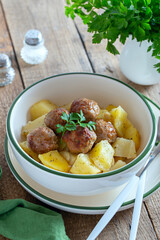 Potatoes with meatballs in a bowl on a wooden table, selective focus