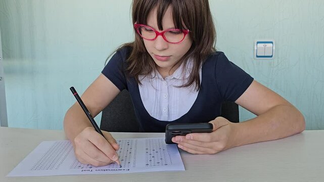 Student child holding smartphone during control exam test at school and cheating on the exam. Write off cheat sheet in lesson or exam