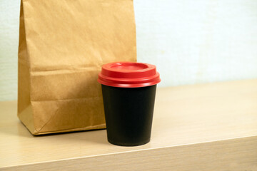 Takeaway food. Black cup with red lid with coffee and paper bag with food