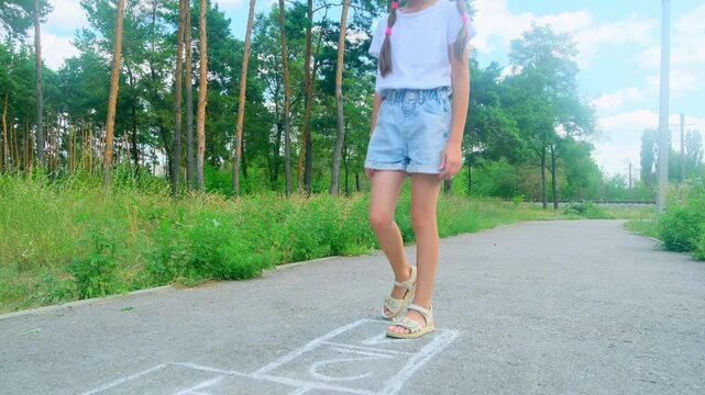 Cute adorable little young child girl playing hopscotch outdoor. Funny activity game for kids on playground outside. Summer backyard street sport for children. Happy childhood lifestyle.