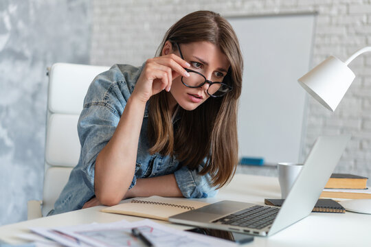 Close up portrait of a young business analyst woam or economy student sitting at the office desk and lookig at laptop monitor with anxious worried face expression
