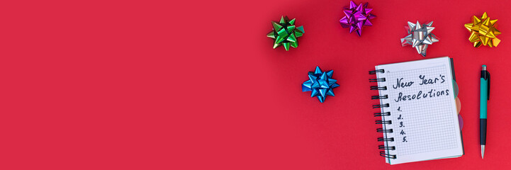Banner of New Year's resolutions concept. Writing in a notebook New Year's resolutions on red background with bows. Flat lay. Top view