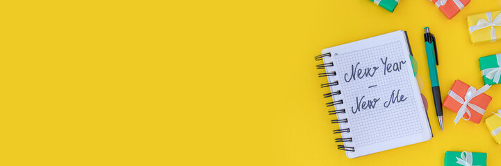 Banner of Christmas background. notebook with the inscription new year - new me on a yellow background with a pen and colorful gifts. flat lay. top view