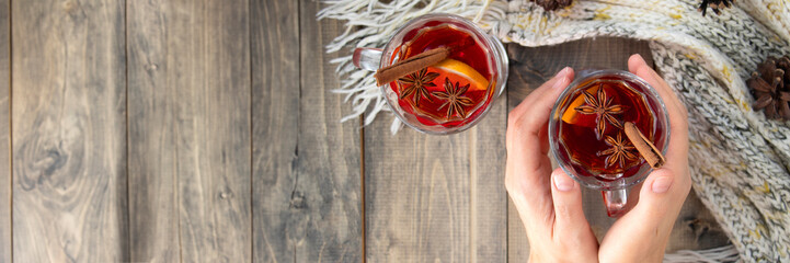 Banner of female hands hold a glass of hot punch. mulled wine on a wooden table next to a warm knitted scarf. a warming drink in winter or autumn. Soft focus. view from above. flat lay