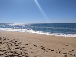 A serene beach at midday with gentle waves lapping the shore and clear blue skies inviting...