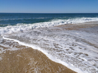 A serene beach at midday with gentle waves lapping the shore and clear blue skies inviting relaxation