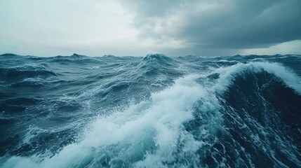 Fototapeta premium Waves crashing in a vast ocean under a cloudy sky on a dramatic day.