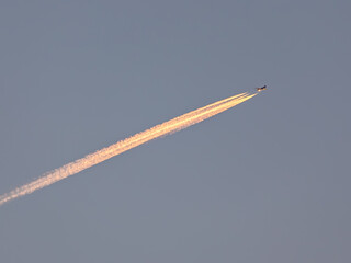 A plane flies through a clear sky, leaving a smoke trail behind