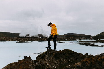 Obraz premium Person In Yellow Jacket Stands On Rugged Terrain By Water.