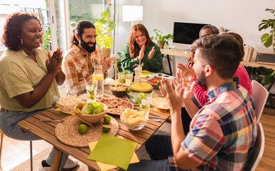 Group of friends clapping hands sitting around table at home