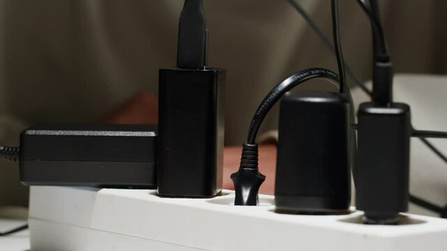 White power strip with many various of cords and cables in close-up. An extension cord with many power sockets. Adapter with phone, headphones, usb connectors.Tangled wires on table. Trying to