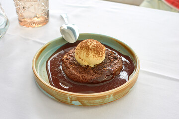 Cookie with chocolate sauce with a scoop of vanilla ice cream on a green plate on the white tablecloth of a restaurant table