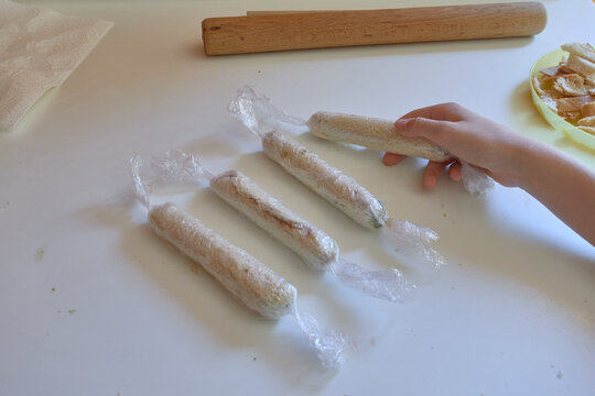 Female hand taking a roll from a slice of chocolate filled bread wrapped in cling film to prepare homemade cinnamon rolls