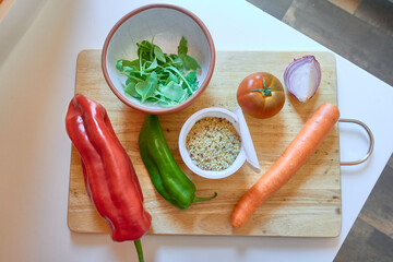 Ingredients to prepare a salad on a wooden cutting board on white countertop: plastic container...