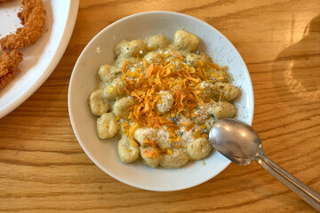 Overhead view of a plate of gnocchi pasta with butter and sage sauce accompanied by sweet potato crisp, with two spoons on a wooden table