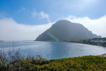 Scenic view of Morro Rock calm ocean waters, surrounded by lush greenery in Morro Bay, California