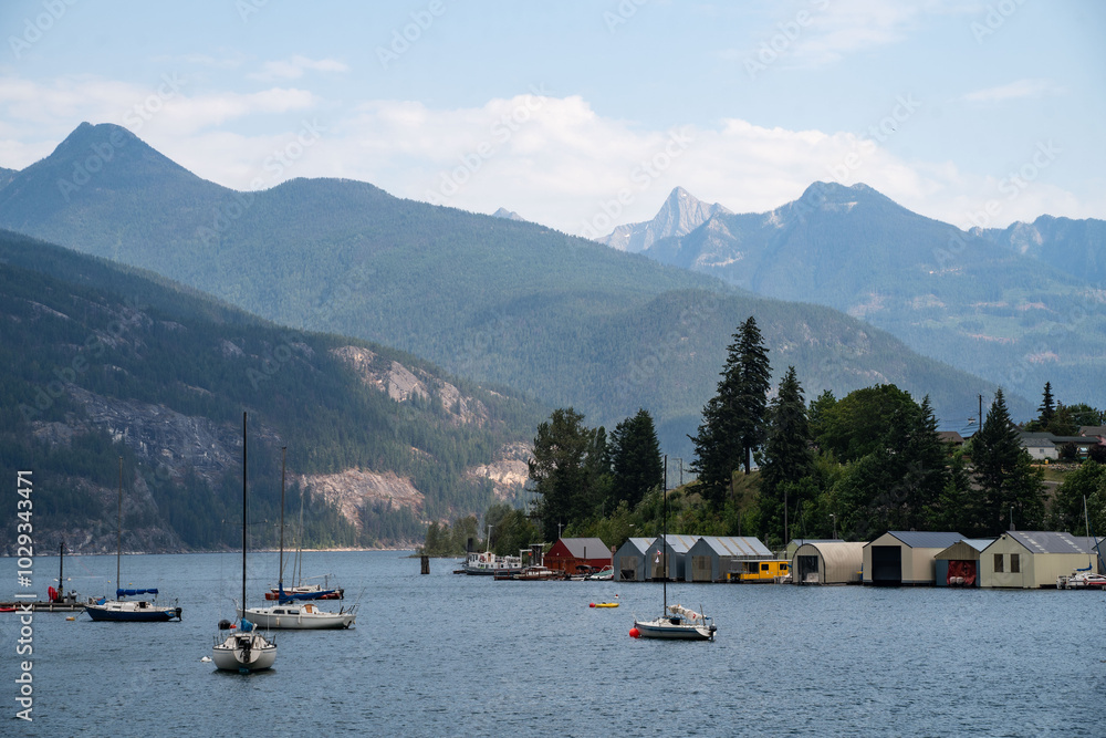 Wall mural tranquil lake view with colorful boats and wooden cabins against a backdrop of mountains on a sunny 