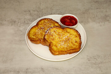 Two pieces of French toast and strawberry syrup on the side served on a white plate.