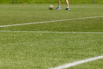 Football pitch with synthetic grass, with white lines on the lower two thirds, and the feet of an athlete with a ball on the upper third.