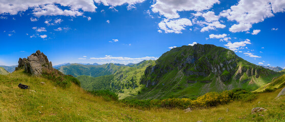Panoramic view of a valley from a mountain peak , In the foreground a rock and a backpack on the ground.