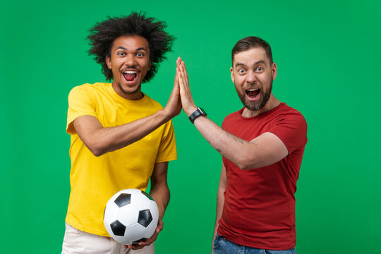 Studio shot of two buddies young soccer fans cheering up and celebrating triumph giving each other high five, isolated over green background