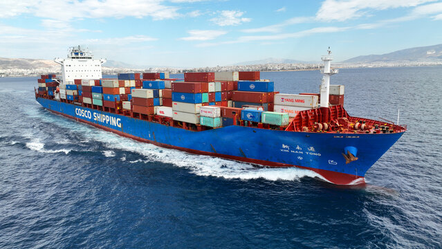 Aerial drone ultra wide photo of COSCO truck size container ship cruising in deep blue sea near commercial port of Piraeus