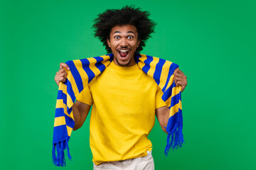 Portrait of excited happy smiling young african american soccer supporter man in basic t-shirt and yellow-blue scarf cheering for his favourite team