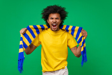 Studio portrait of euphoric screaming young soccer supporter man in basic t-shirt and yellow-blue scarf cheering for his favourite team