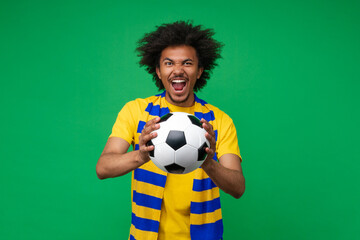 Studio portrait of euphoric soccer supporter young man wearing yellow-blue scarf posing over green...