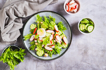 Light salad of crab sticks, cucumber, boiled egg and lettuce on a plate on the table top view