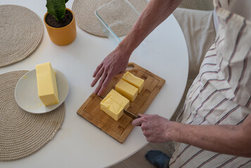 human hand cutting butter on a wooden board in the kitchen at home