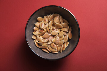Yellow pumpkin seeds on a red background, top view