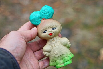 one small gray rubber beautiful funny children's toy old with red lips and green bow on head doll girls in hand man daytime outdoors