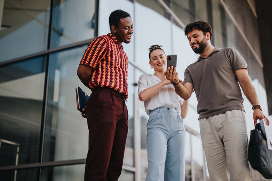 Three business people collaborate outdoors in an urban city, engaging in discussion and sharing ideas while looking at a smart phone.