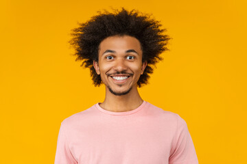 Close up studio portrait of young attractive African American man in basic pastel pink t-shirt posing over yellow background