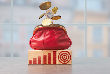A red purse overflowing with coins positioned on wooden blocks representing financial growth and...