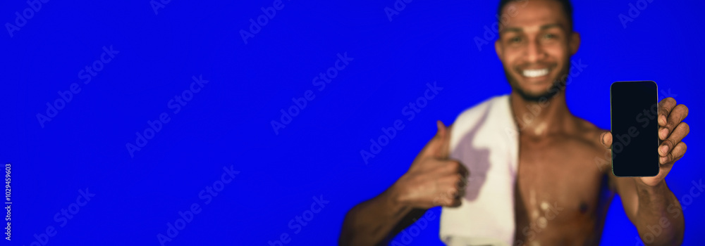 Poster Workout Application. Athlete Guy Showing Smartphone Blank Screen Gesturing Thumbs-Up Standing On Blue Studio Background. Mockup, Shallow Depth