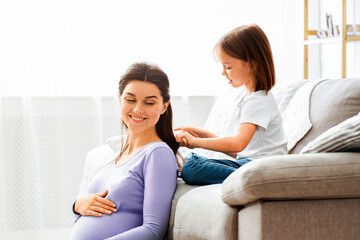 Obraz premium Cute little girl brushing her smiling pregnant mom hair, home interior, free space