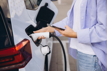 Woman Charging Electric Car While Using Smartphone at Modern Charging Station