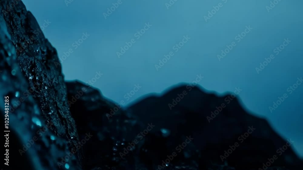 Poster dark, wet rock is illuminated by the sun, creating a stark contrast against the vivid blue sky. the 