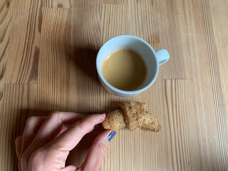 Minimalist wooden table with white cup of fresh espresso and female hand holding small croissant, perfect for cozy breakfast or cafe related images