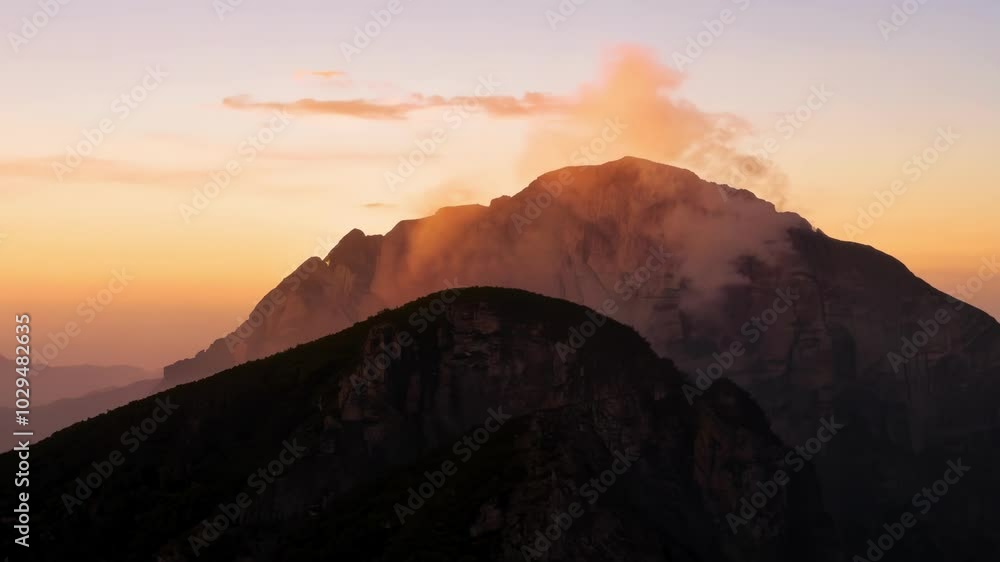 Poster The last rays of sun are illuminating the peak of a mountain, surrounded by clouds, creating a magical and evocative atmosphere
