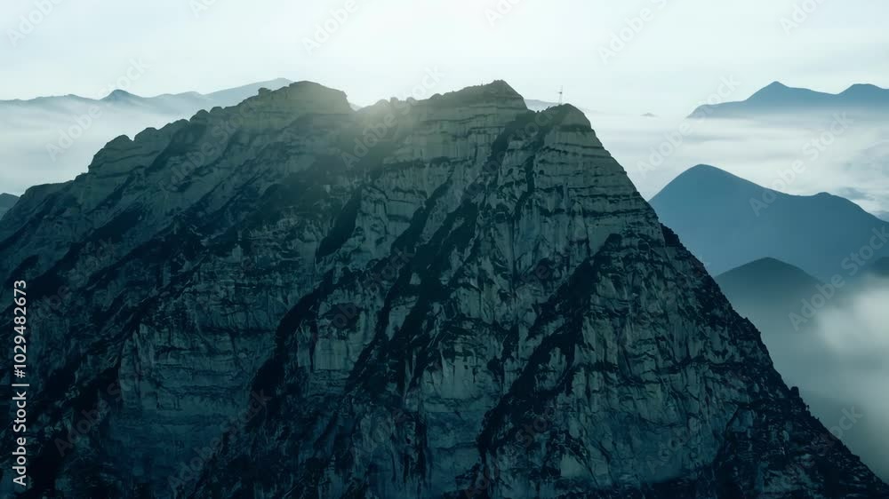 Aufkleber Majestic mountain peak rises above the clouds on a foggy morning, with soft dawn light highlighting rugged cliffs and slopes in a serene landscape
