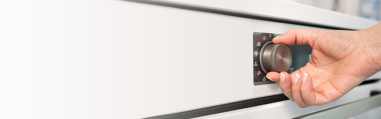 Woman adjusting modern white oven in kitchen.  Female hand pushing and turning knobs on oven control panel. Long banner